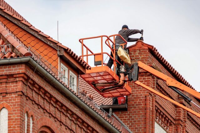 Roofer inspecting a tiled roof A roofer on a lift inspecting a tiled roof on a brick building