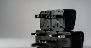Stack of black electrical plug adapters with different pin types on a grey surface