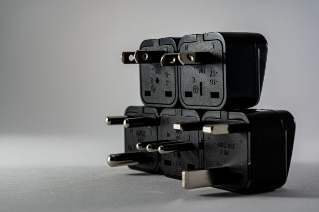 electrical-safety-at-work-what-is-competence-why-it-matters Stack of black electrical plug adapters with different pin types on a grey surface