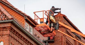 Roofer on a cherry picker repairing the tiled roof of a red brick building
