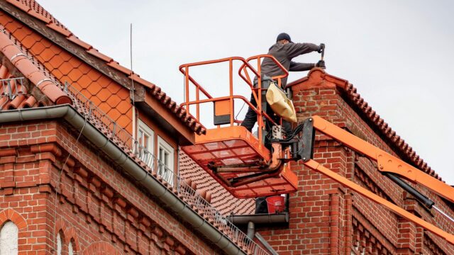 Roofer in Harrogate Roofer on a cherry picker repairing the tiled roof of a red brick building